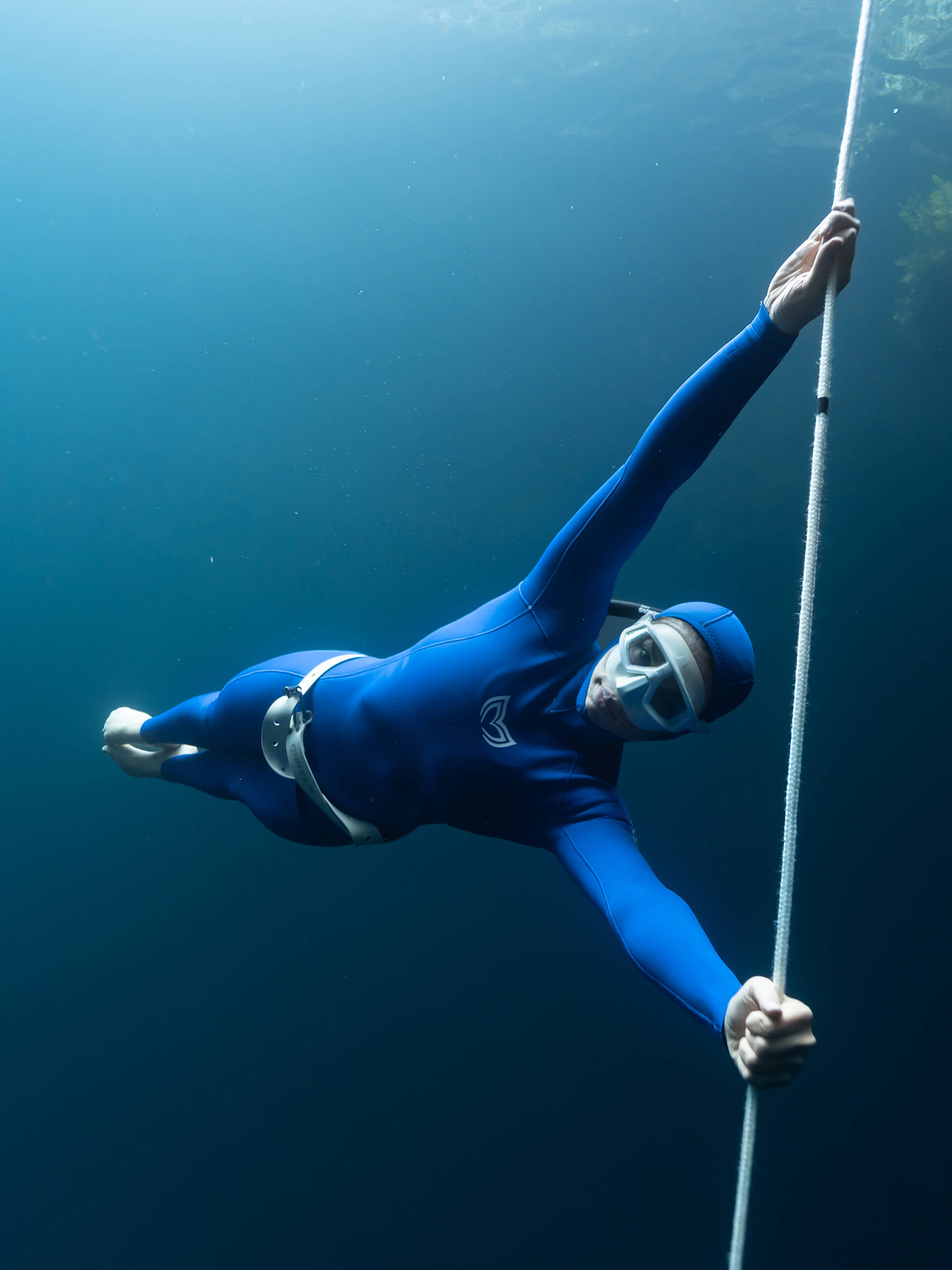 Image of a female diver hanging from a dive line wearing a blue 2.5mm/4.5mm double lined womens freediving wetsuit