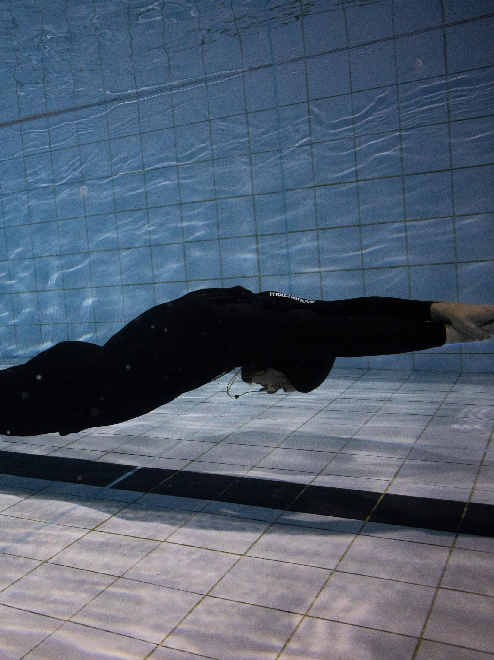 A male athlete completing a dynamic dive in a pool while wearing a 1.5mm smooth skin wetsuit.