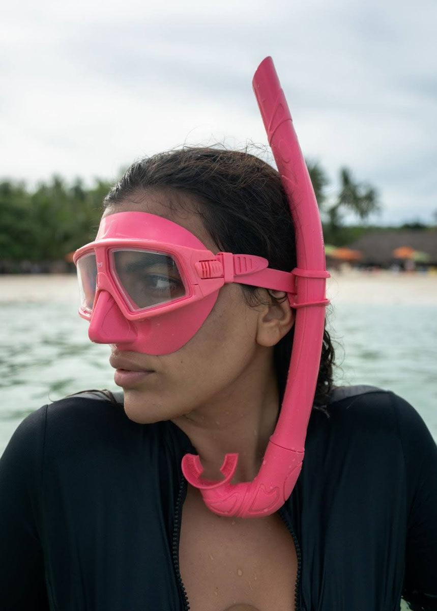 Woman wearing a pink freediving snorkel and mask above water near tropical beach